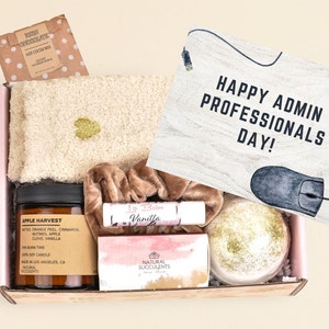 May include: A pink gift box filled with various items, including a candle, bath bomb, and a fuzzy slipper. The box is topped with a card that reads "Happy Admin Professionals Day!" and a mousepad with a computer mouse illustration.