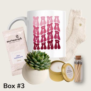 Puede incluir: Una caja de regalo con una taza blanca con el texto "MAMA" repetido en una fuente retro en rosa y rojo. La caja tambi&eacute;n incluye una peque&ntilde;a planta suculenta, una vela, un peque&ntilde;o frasco de cerillas y un par de calcetines blancos peludos.