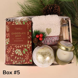 May include: Gift box with a variety of items. Includes a box of chocolate chip cookies, a plush beige towel with a gold heart, a candle, a bath bomb, and matches. The box is labeled "Box #5".