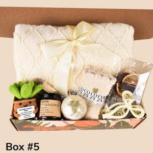May include: A gift box with a cream-colored blanket tied with a yellow ribbon. The box contains a crocheted succulent, candle, bath bomb, socks, hair clip, and a snack. The box is labeled "Box #5".
