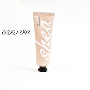 May include: A pink tube of hand cream with the word "shea" written in white cursive on the front. The tube has a black cap.