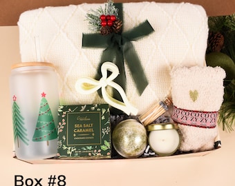 Könnte beinhalten: Eine Geschenkbox gefüllt mit einer cremefarbenen Decke, einem Glas mit Weihnachtsbaum-Designs, einer Keksschachtel, einer Kerze, einer Badekugel und einem kleinen Handtuch. Die Box ist mit einem grünen Band gebunden und mit Tannenzapfen und Beeren verziert. Der Text auf der Box lautet "Box #8".