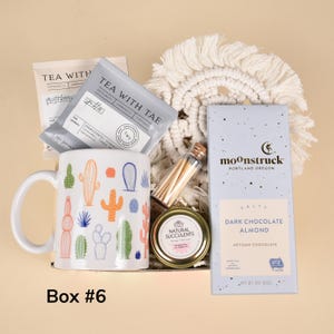May include: A gift box with a white mug decorated with colorful cacti, tea packets, a small jar, a matchstick container, a macrame coaster, and a blue box of dark chocolate almond. The text "Box #6" is at the bottom.