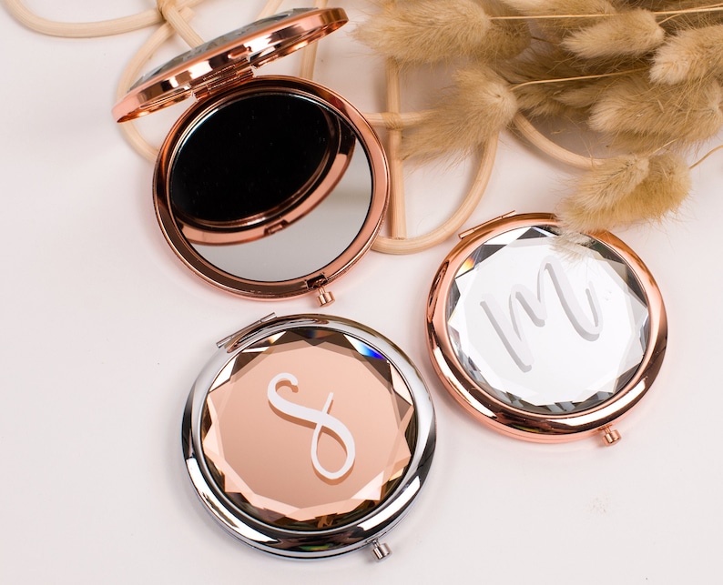 May include: Three rose gold compact mirrors with a clear glass surface. The mirrors have a diamond-shaped design and are engraved with the letters "S", "M", and "I".