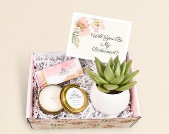 May include: A pink and white gift box with a succulent plant, a candle, matches, and a card that says "Will You Be My Bridesmaid?"