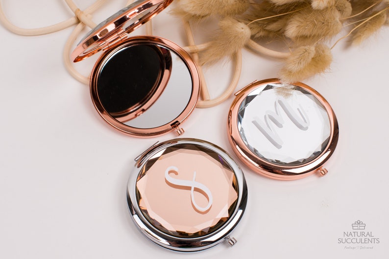 May include: Three round, rose gold compact mirrors with a faceted design. The mirrors have a silver trim and are engraved with different initials.