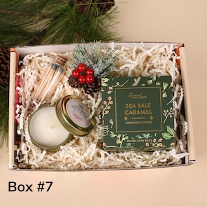 May include: Gift box with a candle, matches, cookies, and decorative accents. The candle is in a gold tin with the words "Natural Succulent". The cookie box is green with the words "Sea Salt Caramel". The box is labeled "Box #7".