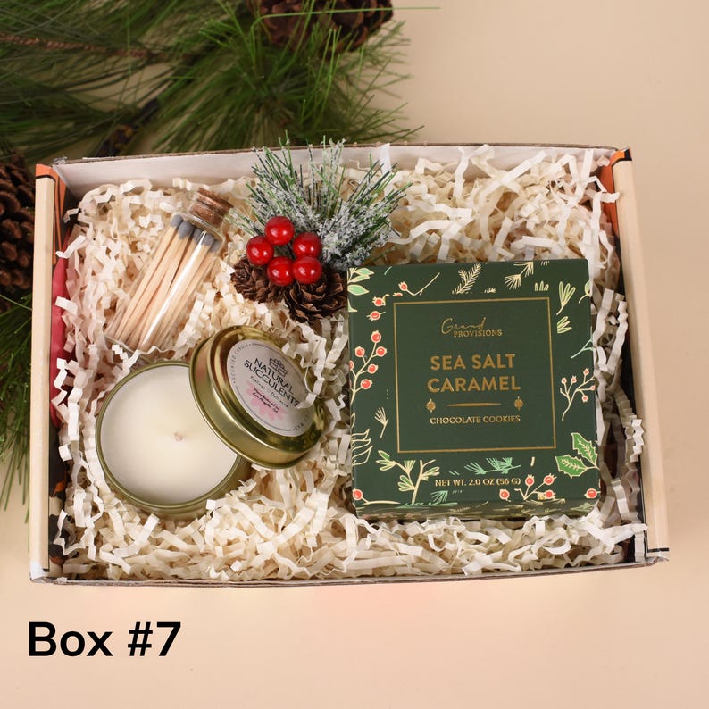 May include: Gift box with a candle, matches, cookies, and decorative accents. The candle is in a gold tin with the words "Natural Succulent". The cookie box is green with the words "Sea Salt Caramel". The box is labeled "Box #7".