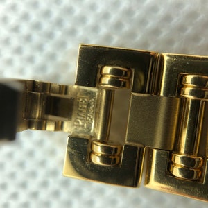 May include: Close-up of a gold watch band with the words "SWISS MADE" and "PLATINUM" engraved on the clasp.
