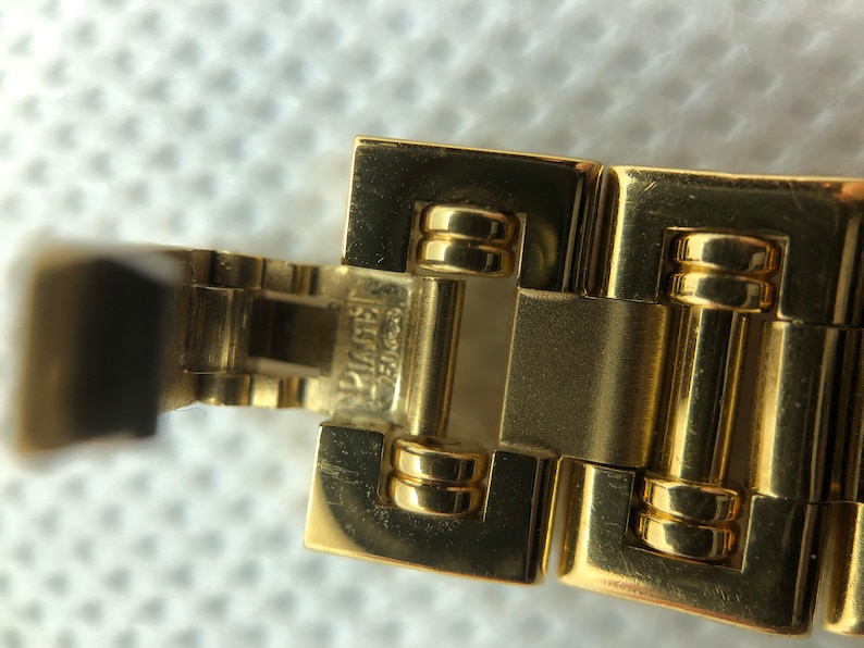 May include: Close-up of a gold watch band with the words "SWISS MADE" and "PLATINUM" engraved on the clasp.