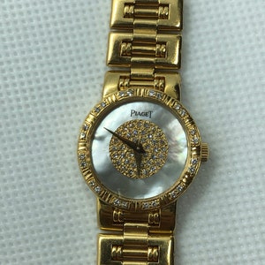 May include: A gold Piaget watch with a white mother-of-pearl face and diamond accents. The watch has a gold band.