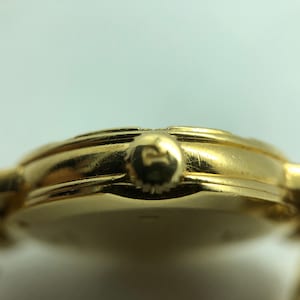 May include: A gold-toned wristwatch with a round face and a metal band. The watch has a small crown on the side.