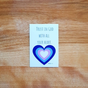 May include: A white card with blue text that reads "TRUST IN GOD WITH ALL YOUR HEART."  The card has a blue, pink, and white heart with the verse "Proverbs 3:5-6" at the bottom.