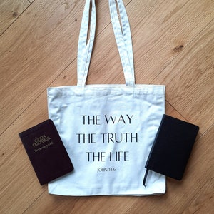 May include: White canvas tote bag with the text "THE WAY THE TRUTH THE LIFE JOHN 14:6" printed on it. A burgundy book with the text "GOD'S PROMISES for your every need" is on the left side of the bag and a black notebook is on the right side of the bag.