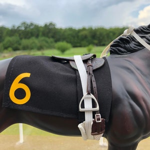 May include: A black horse with a white saddle and a black and yellow racing number 6 on its side.