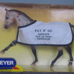 May include: A Breyer model horse named "Pay N' Go" is in a box. The horse is a brown and white Appaloosa with a white blanket that says "Pay N' Go Appaloosa Hall of Fame Dressage".
