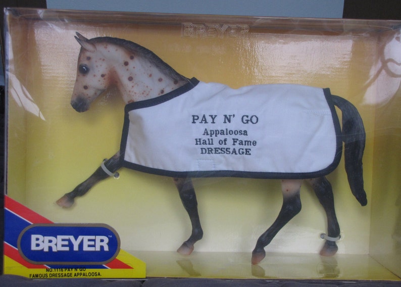 May include: A Breyer model horse named "Pay N' Go" is in a box. The horse is a brown and white Appaloosa with a white blanket that says "Pay N' Go Appaloosa Hall of Fame Dressage".