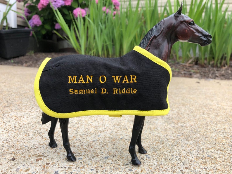May include: Black horse figurine wearing a black and yellow horse blanket with the text "MAN O WAR Samuel D. Riddle" embroidered on it.