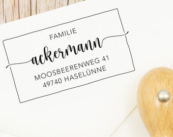 Könnte beinhalten: Ein selbsttinte­nder Stempel aus Holz mit einem schwarzen rechteckigen Rahmen und dem Text "Familie Ackermann Moosbeerenweg 41 49740 Haseluenne" im Inneren.