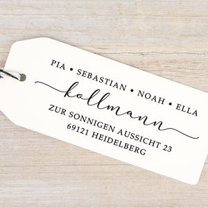 Könnte beinhalten: Ein weißes, rechteckiges Geschenkanhänger-Etikett mit abgerundeten Ecken und einer schwarz-weißen Schnur. Das Etikett zeigt schwarzen Text: PIA • SEBASTIAN • NOAH • ELLA, den Namen "kollmann" in Schreibschrift und die Adresse ZUR SONNIGEN AUSSICHT 23 69121 HEIDELBERG.