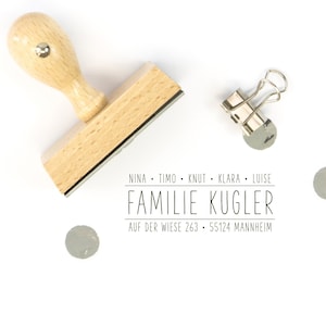Pu&ograve; includere: Timbro in legno con manico e base rettangolare. Il timbro recita "Nina. Timo. Knut. Klara. Luise. Familie Kugler. Auf der Wiese 263. 55124 Mannheim."