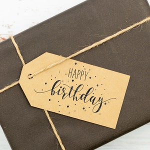 May include: A brown paper gift bag with a brown twine bow and a gift tag that says "Happy birthday."