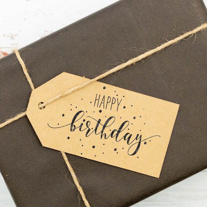 May include: A brown paper gift bag with a brown twine bow and a gift tag that says "Happy birthday."