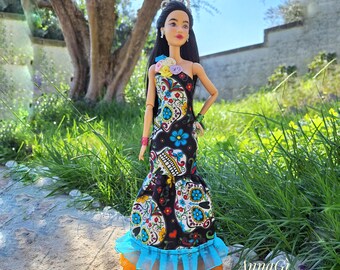 Puede incluir: Una muñeca con cabello largo negro que lleva una corona plateada y un vestido negro de un solo hombro con un patrón colorido de calaveras de azúcar, detalles florales en el hombro y un dobladillo con volantes azul y naranja.