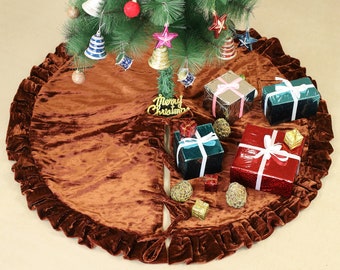 Puede incluir: Una falda de árbol de Navidad de terciopelo marrón con un borde con volantes. La falda está decorada con purpurina dorada y las palabras "Merry Christmas". Hay varios regalos envueltos y adornos en la falda.