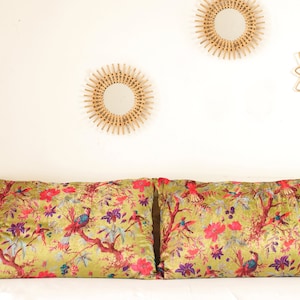 May include: Two decorative throw pillows with a vibrant floral and bird pattern. The pillows feature a golden-green background with red, pink, purple, and blue accents. The pillows are rectangular in shape and rest on a wooden headboard.