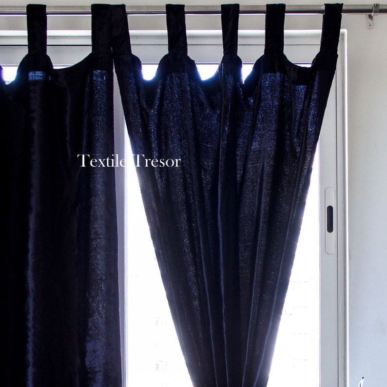 Puede incluir: Cortinas de terciopelo azul oscuro con una barra blanca y un marco de ventana blanco. Las cortinas est&aacute;n reunidas en la parte superior y tienen un detalle de borla decorativo. El texto "Textile Tresor" es visible en las cortinas.