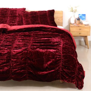 Peut inclure: Ensemble de literie en velours rouge foncé. L'ensemble comprend une couette et deux taies d'oreiller. La couette et les taies d'oreiller présentent un design froncé, ajoutant de la texture. L'ensemble est présenté sur un cadre de lit en bois.