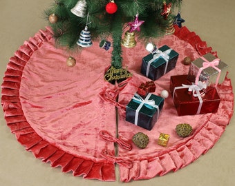 May include: A pink velvet Christmas tree skirt with a ruffled edge. The skirt is decorated with a gold "Merry Christmas" sign and several wrapped gifts.