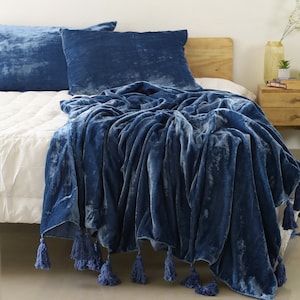 May include: A blue velvet throw blanket with tassels on a bed with blue pillows.