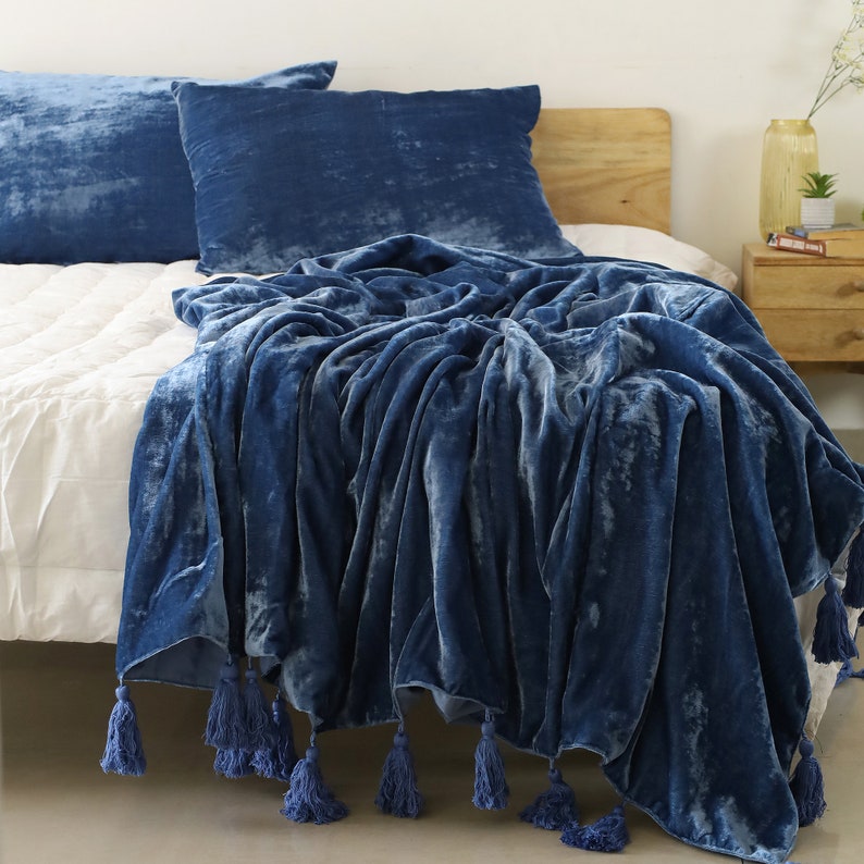 May include: A blue velvet throw blanket with tassels on a bed with blue pillows.