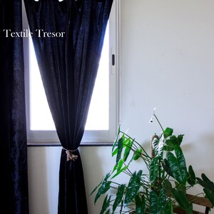 Puede incluir: Cortinas negras con un amarre de cuerda colgando en una ventana. Las cortinas est&aacute;n hechas de una tela suave y texturizada. Una planta verde en una cesta de mimbre est&aacute; en primer plano.
