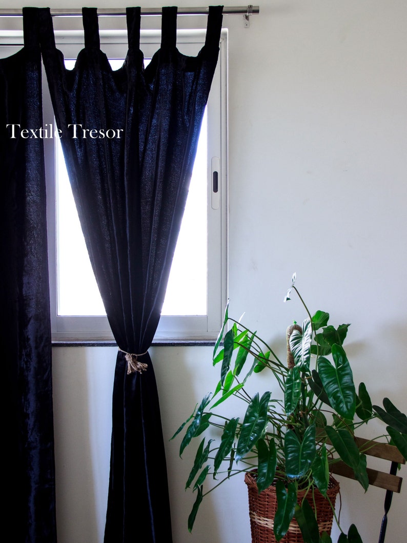 Puede incluir: Cortinas negras con un amarre de cuerda colgando en una ventana. Las cortinas est&aacute;n hechas de una tela suave y texturizada. Una planta verde en una cesta de mimbre est&aacute; en primer plano.