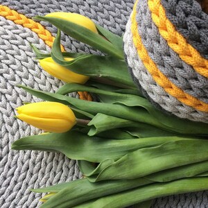 May include: A bunch of yellow tulips with green leaves on a grey knitted rug with yellow stripes.