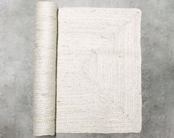 Puede incluir: Una alfombra rectangular de yute blanca enrollada sobre un fondo de hormigón gris.
