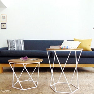 May include: A dark blue sofa with white and yellow throw pillows sits in a living room with two white metal side tables with wooden tops. The sofa is on a light brown rug.