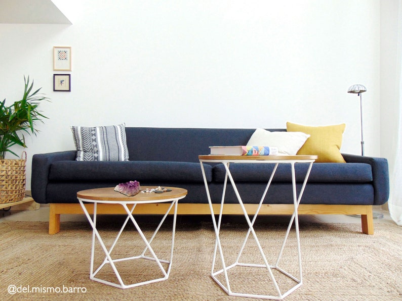 May include: A dark blue sofa with white and yellow throw pillows sits in a living room with two white metal side tables with wooden tops. The sofa is on a light brown rug.