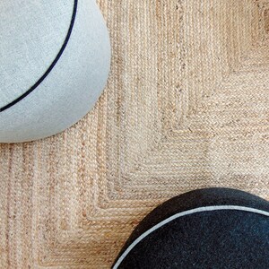 May include: Two round, gray and black poufs with white trim sit on a natural jute rug with a woven pattern.