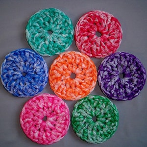 May include: Seven crocheted scrubbers in different colors, including green, red, blue, orange, purple, and pink. Each scrubber has a white center and is shaped like a donut.