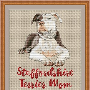 May include: Cross stitch pattern of a white and brown Staffordshire Terrier dog sitting with its paws crossed. The text "Staffordshire Terrier Mom" is below the dog in red.