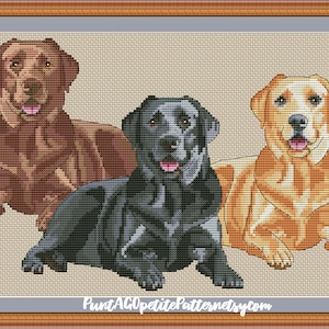May include: Cross stitch pattern of three Labrador Retrievers. One is brown, one is black, and one is yellow. The dogs are sitting and looking at the viewer.
