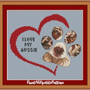 May include: Cross-stitch pattern featuring a red heart and a dog paw print. The text "I LOVE MY AUSSIE" is inside the heart. The paw print is brown and white. The background is light blue.