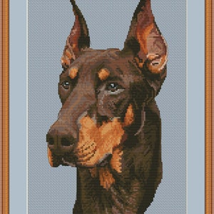 May include: A cross-stitch pattern of a brown and tan Doberman Pinscher dog with cropped ears. The dog is looking to the left of the image. The pattern is on a light blue background.