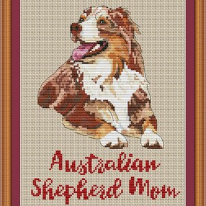 May include: Cross-stitch pattern of an Australian Shepherd dog sitting with its tongue out. The pattern is framed in a brown and red frame. The text "Australian Shepherd Mom" is below the dog and the website "PuntAGOpetitePatternetsy.com" is below the text.