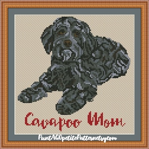May include: Cross stitch pattern of a black and grey dog with the text "Cavapoo Charm" in red.