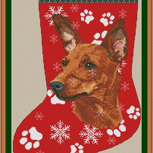 May include: A red Christmas stocking cross-stitch pattern featuring a brown Pinscher dog portrait, white snowflake motifs, and white paw prints. The top cuff displays the text PINSCHER in black letters, with a decorative border above and below.